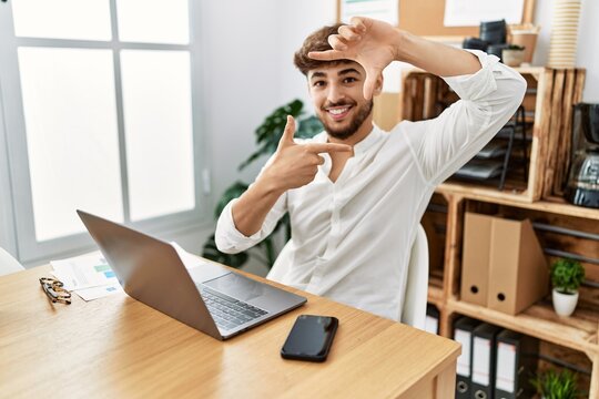 Young arab man working using computer laptop at the office smiling making frame with hands and fingers with happy face. creativity and photography concept.