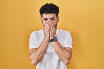 Arab man standing over yellow background shocked covering mouth with hands for mistake. secret concept.