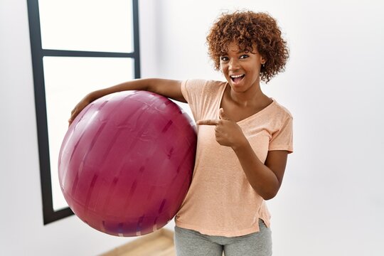 Young african american woman holding pilates ball smiling happy pointing with hand and finger