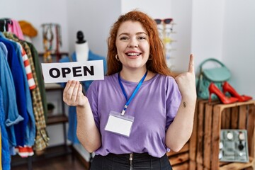 Fototapeta na wymiar Young redhead woman holding banner with open text at retail shop smiling with an idea or question pointing finger with happy face, number one