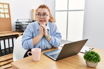Young redhead woman working at the office using computer laptop laughing nervous and excited with...