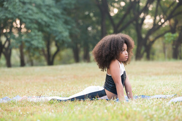 Child little girl doing meditate yoga asana on roll mat with eyes closed in park. Kids girl practicing doing yoga outdoor