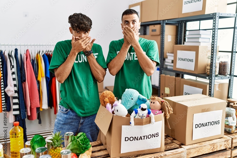 Canvas Prints Young gay couple wearing volunteer t shirt at donations stand shocked covering mouth with hands for mistake. secret concept.