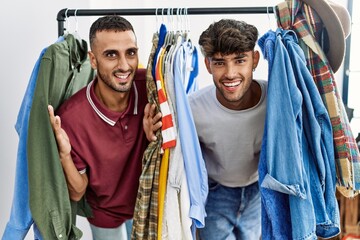 Young hispanic man smiling happy appearing through clothes at clothing store.