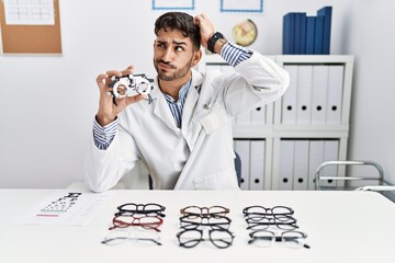 Young optician man holding optometry glasses confuse and wondering about question. uncertain with...