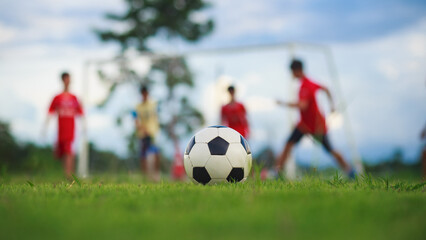 Action sport outdoors of group of kids having fun playing soccer football for exercise in green grass field at community park.