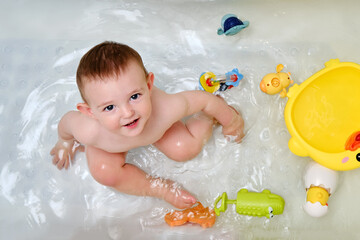 Happy toddler baby boy is playing with toys in the bathtub. A smiling child plays in the water of a...