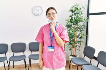 Young asian nurse woman at medical waiting room thinking concentrated about doubt with finger on...