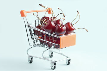 Miniature shopping cart full of ripe red cherries. Buying fruit, healthy food, vitamins.