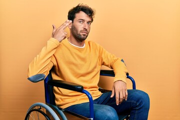 Handsome man with beard sitting on wheelchair shooting and killing oneself pointing hand and fingers to head like gun, suicide gesture.