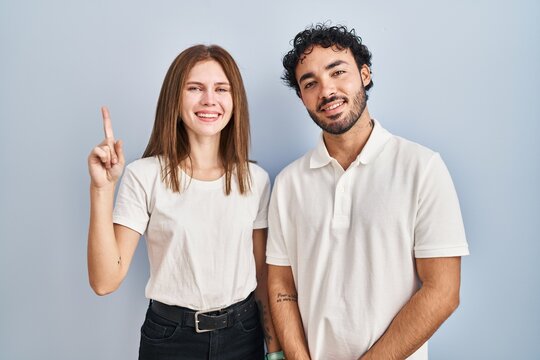 Young couple wearing casual clothes standing together showing and pointing up with finger number one while smiling confident and happy.
