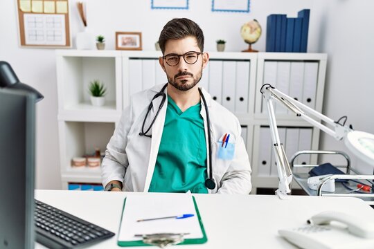 Young man with beard wearing doctor uniform and stethoscope at the clinic skeptic and nervous, frowning upset because of problem. negative person.