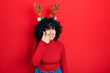 Young middle east woman wearing cute christmas reindeer horns doing happy thumbs up gesture with...