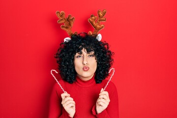 Young middle east woman wearing cute christmas reindeer horns looking at the camera blowing a kiss...