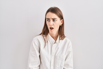 Obraz premium Young caucasian woman standing over isolated background in shock face, looking skeptical and sarcastic, surprised with open mouth