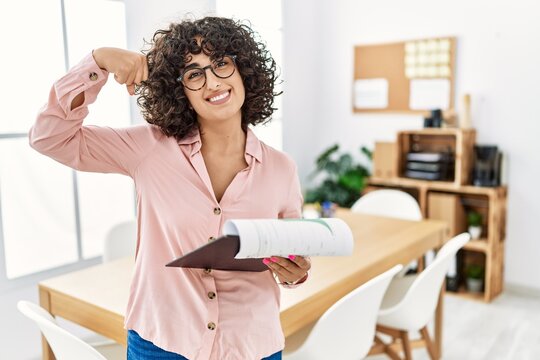 Young middle eastern woman wearing business style at office strong person showing arm muscle, confident and proud of power