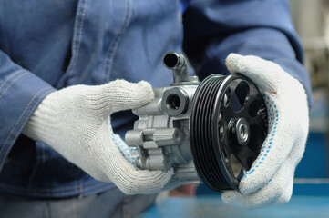 A power steering pump is in the hands of an auto mechanic. Close-up. Compliance and integrity control of the new spare part. Repair and maintenance of a car in a car service center.