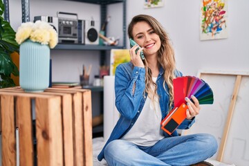 Young woman artist talking on smartphone choosing color at art studio