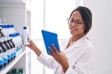 Young hispanic woman pharmacist using touchpad working at pharmacy