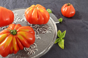 Close up of  awesome ripe slicing tomatoes placed on a decorative glass plate. Dark tablecloth. Different forms.

