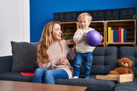 Mother and son playing with ball sitting on sofa at home