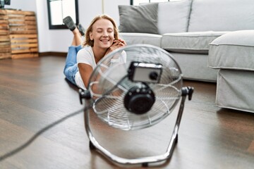 Young blonde woman smiling confident using fan at home