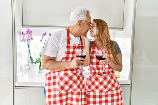 Middle age hispanic couple kissing and drinking wine at the kitchen.