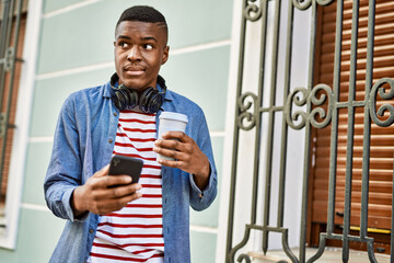 Young african american man using smartphone drinking coffee at the city.