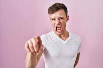Caucasian man standing over pink background pointing displeased and frustrated to the camera, angry...
