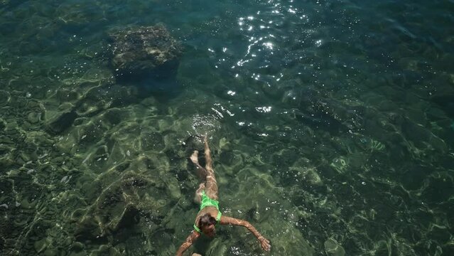 4k slow motion top view of sexy slim woman in green swimsuit floating in clear turquoise water of mediterranean sea close to shore. vacation and wellness, Summer tourist Season Fethiye, Mugla Turkey