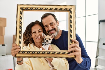 Middle age hispanic family smiling happy holding empty frame at new home.