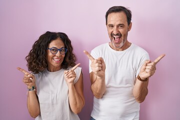 Middle age hispanic couple together over pink background smiling confident pointing with fingers to different directions. copy space for advertisement