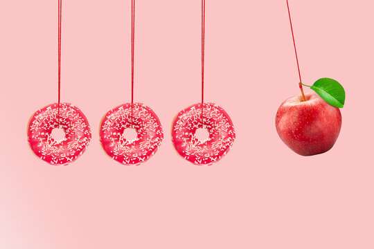 Newton's cradle from doughnuts. Collision balls made from donuts and red apple. Healthy diet concept. Diabetes concept.