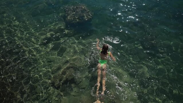 4k slowmotion top view sexy slim woman with nise buttocks in green swimsuit floating in clear turquoise water of mediterranean sea close to shore. vacation and wellness, Summer Season Fethiye, Turkey