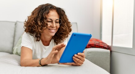 Middle age hispanic woman smiling confident using touchpad at home