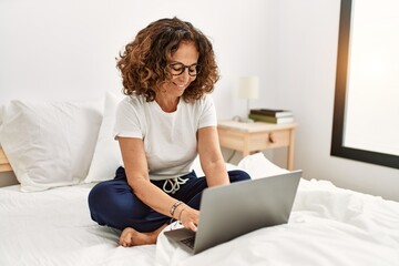 Middle age hispanic woman smiling confident using laptop at bedroom