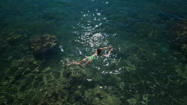 4k slowmotion top view sexy slim woman with nise buttocks in green swimsuit floating in clear turquoise water of mediterranean sea close to shore. vacation and wellness, Summer Season Fethiye, Turkey