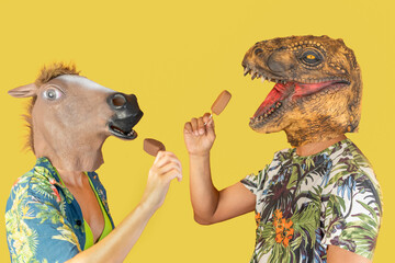 Man in dinosaur animal head mask and woman with horse head eating chocolate ice creams isolated on...