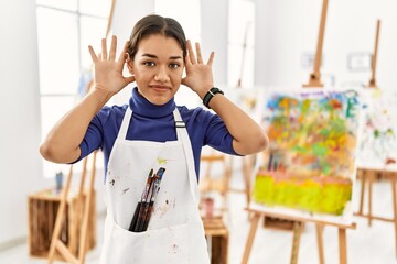 Young brunette woman at art studio trying to hear both hands on ear gesture, curious for gossip. hearing problem, deaf