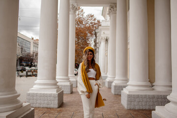 Beautiful woman dressed white jeans, sweater and yellow scarf and beret walking in the street of...