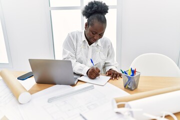 Young african american woman architect using laptop writing on notebook at architecture studio