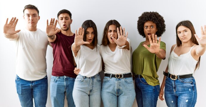 Group of young friends standing together over isolated background doing stop gesture with hands palms, angry and frustration expression