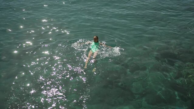 slow motion top view of sexy beautiful young woman in green swimsuit swimming on back and relaxing in clear turquoise water of mediterranean sea. vacation and wellness, Summer Season Fethiye, Turkey