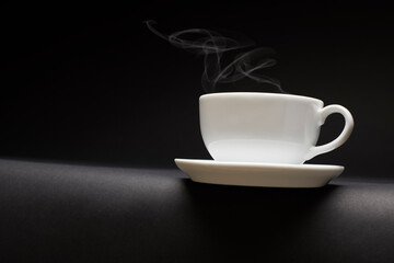 Obraz na płótnie Canvas White ceramic coffee cup with steam on black table.