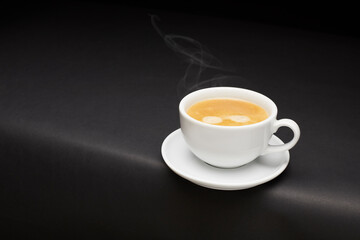 White ceramic coffee cup with steam on black table.