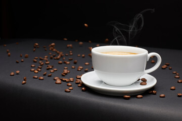 Close up view of flying roasted dark coffee beans near white ceramic cup against black background.