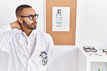 African american optician man standing by eyesight test suffering of neck ache injury, touching neck with hand, muscular pain