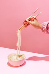 Delicious image of noodles isolated over pink background. Eating japanese cuisine with chopsticks