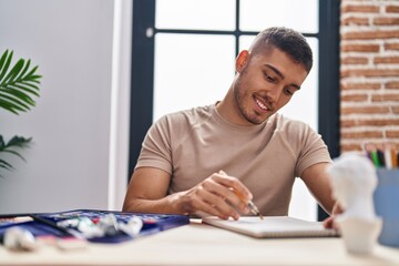 Young hispanic man artist smiling confident drawing on notebook at art studio