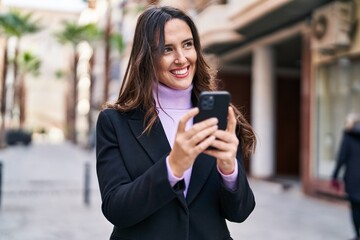 Young hispanic woman smiling confident using smartphone at street